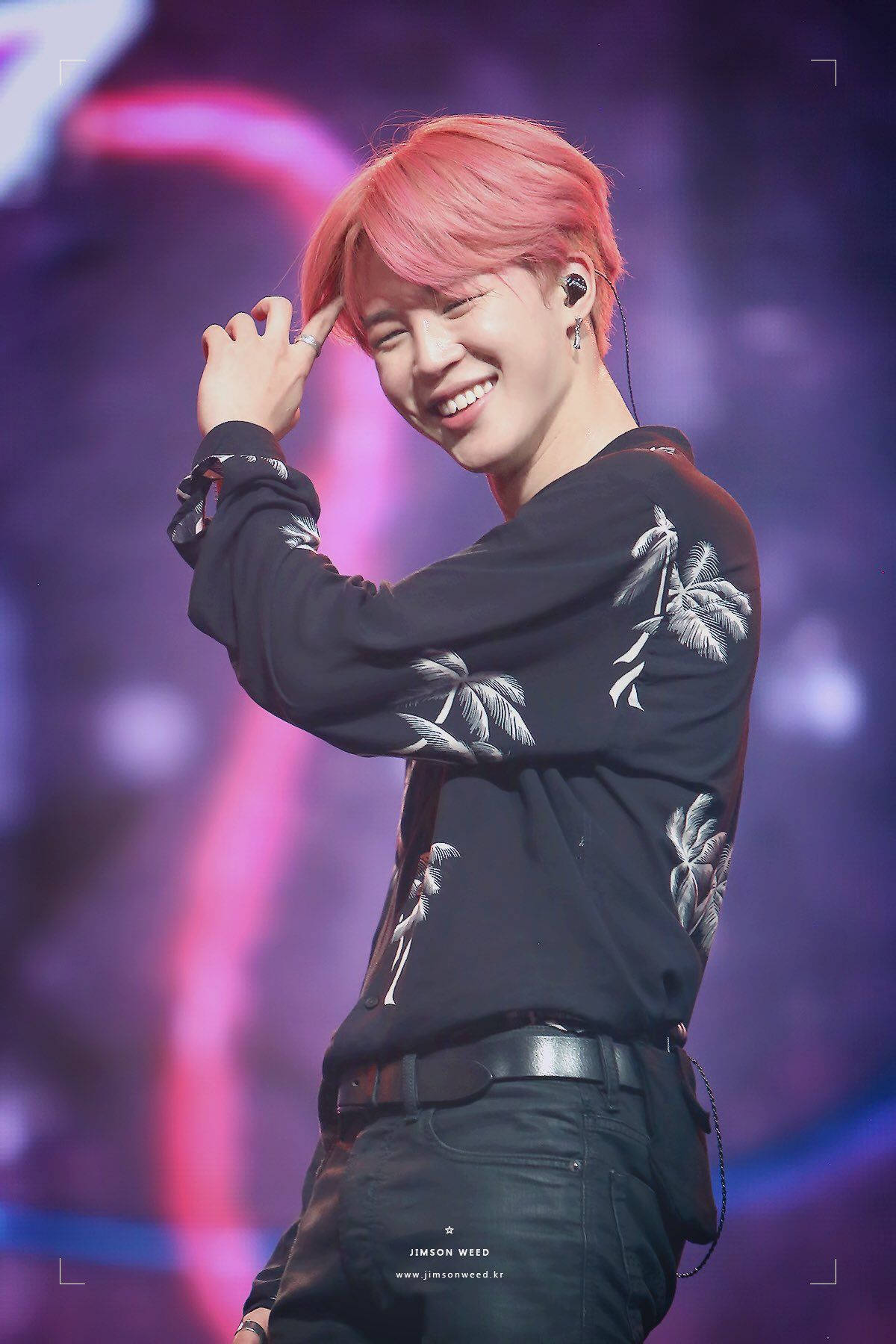 BTS 崔勝哲可愛燦笑 壁紙 — 一位微笑的表演者，粉紅色頭髮和棕櫚樹襯衫，在充滿活力的紫色和粉紅色舞台燈光下跳舞。