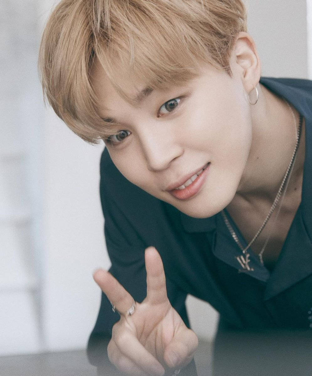 BTS 崔然竣 Rolling Stone 專訪 壁紙 — 一位金髮年輕男子帶著溫暖的笑容，穿著深色襯衫和珠寶，做出和平手勢。