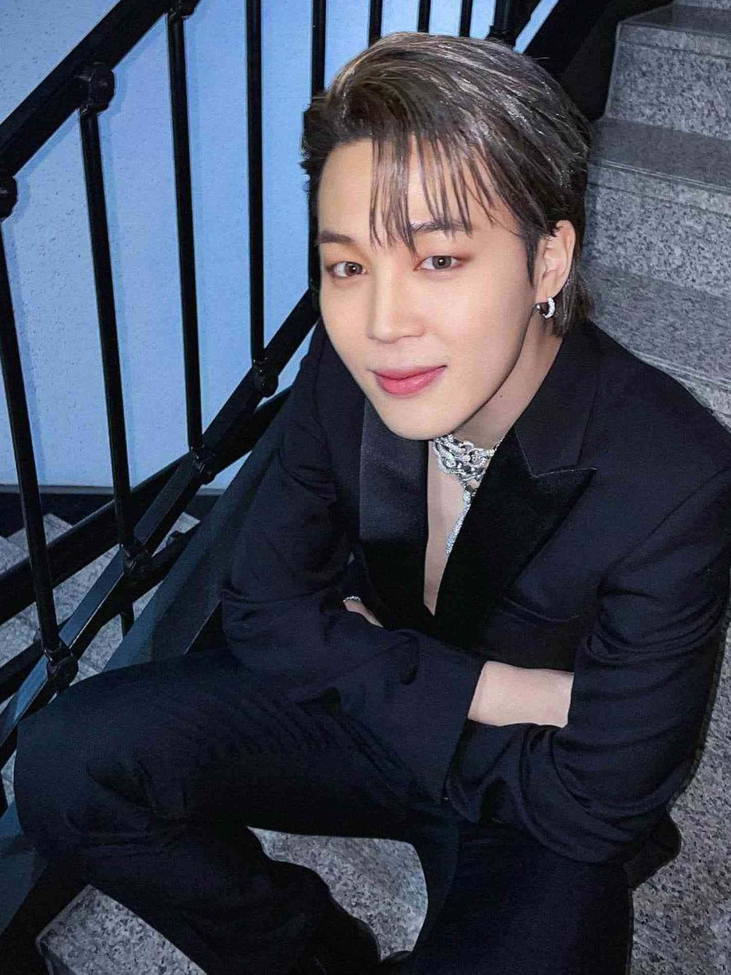 BTS 成員 Jimin 展現經典個人風格 壁紙 — 一位身穿黑色西裝的年輕男子自信地坐在石階上，旁邊有黑色欄杆，在冷藍色燈光下。