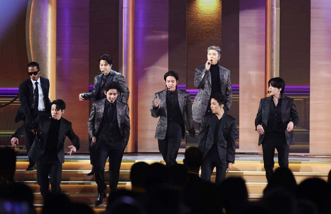 BTS 拉斯維加斯演出照片 壁紙 — 一個K-pop組合在燈光璀璨的舞台上充滿活力地表演，舞台有金色台階和紫色燈光，觀眾的剪影在觀看。