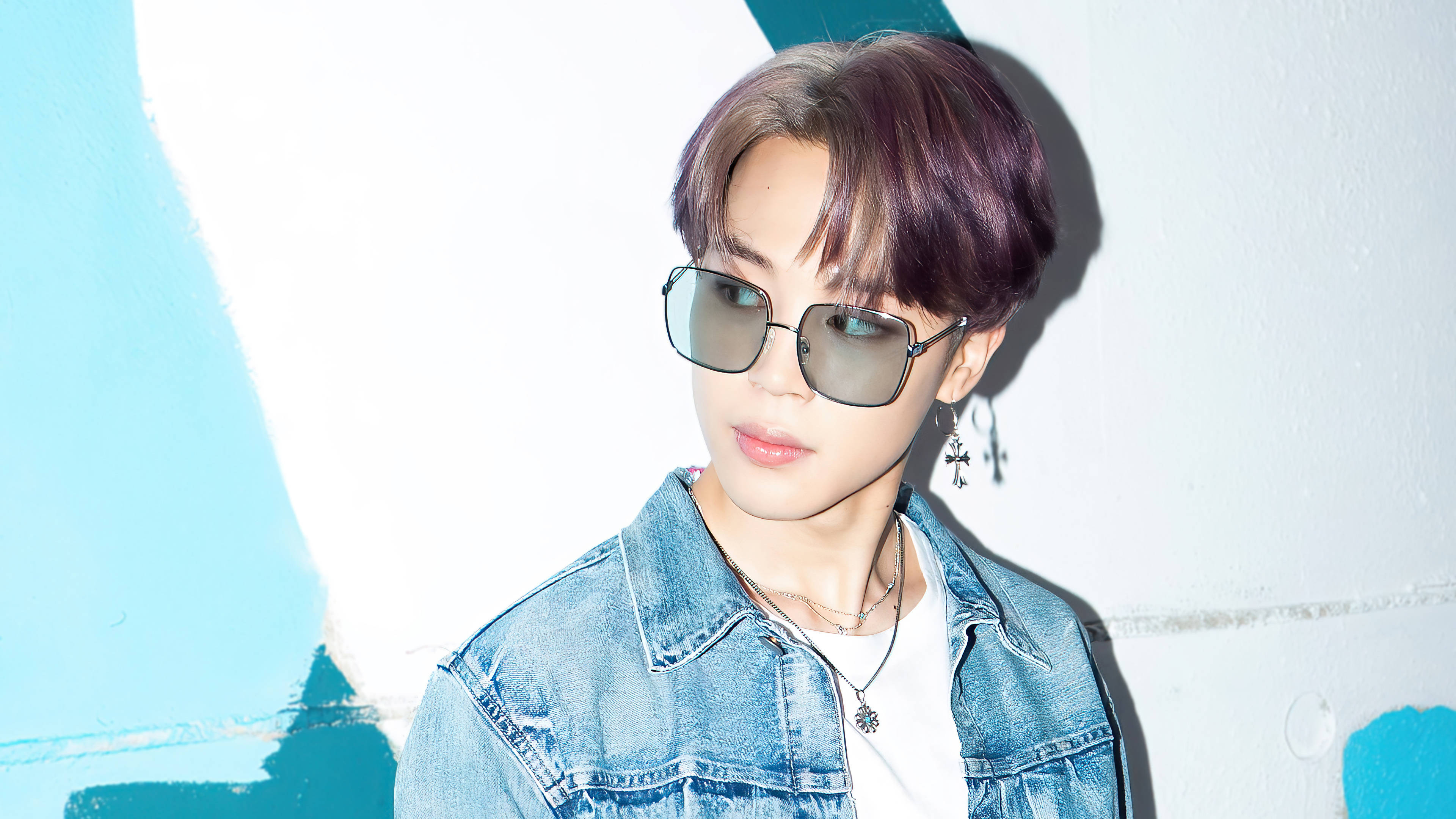 BTS 朴智旻 Dynamite 壁紙 — 一位紫髮戴太陽眼鏡的年輕男子，在帶有藍色塗鴉點綴的白色牆前擺姿勢。