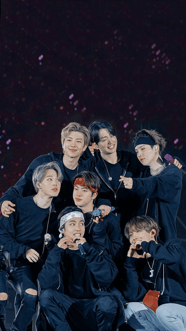 BTS 演唱會美學壁紙 壁紙 — 七位微笑的男性偶像穿著深色服裝在舞台上緊密擺姿勢，閃閃發光的紫色紙屑在他們周圍飄落。