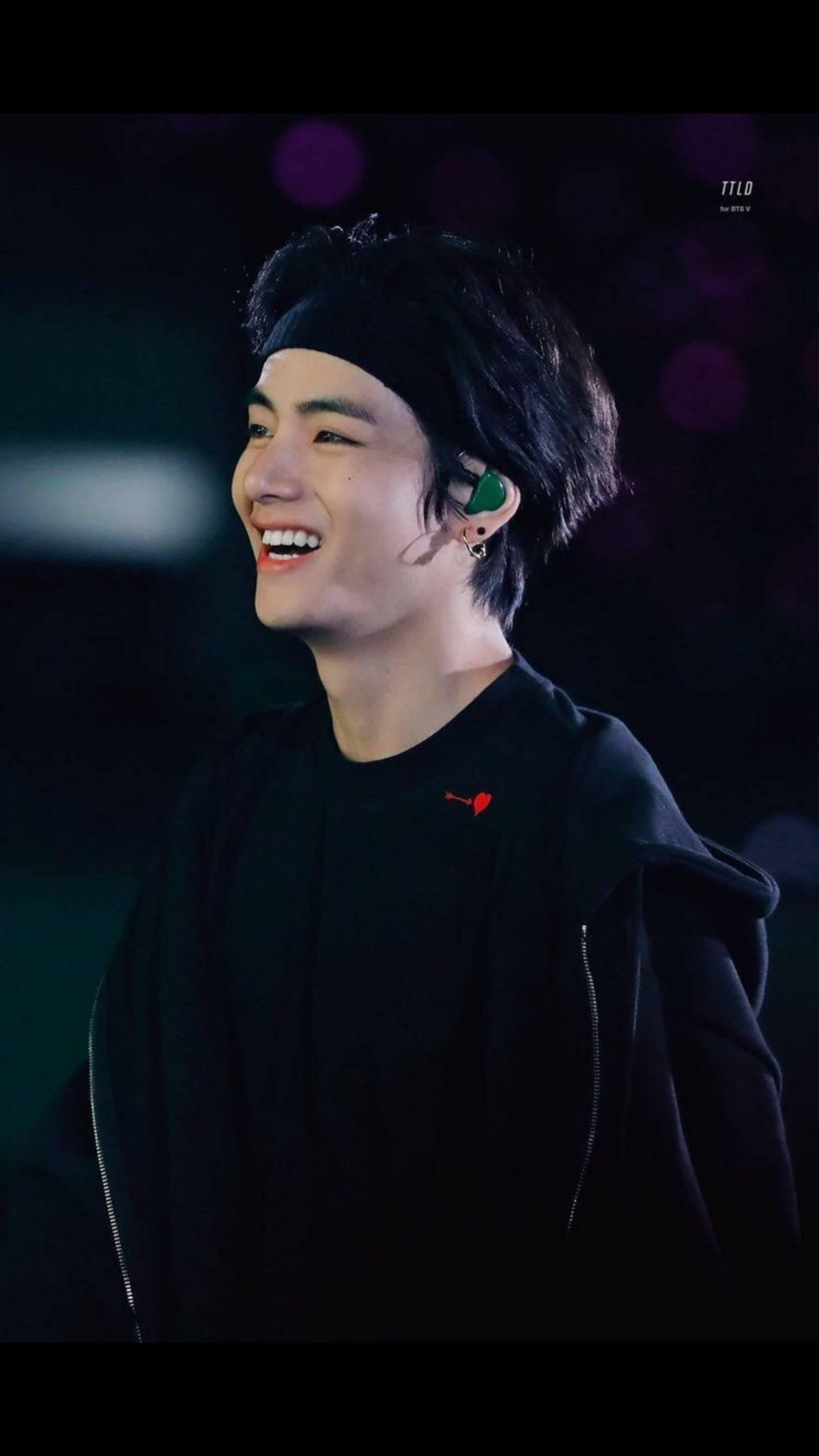 BTS 田柾國 演唱會微笑 壁紙 — 一位黑髮黑衣的年輕男子在紫色舞台燈光下洋溢著喜悅。