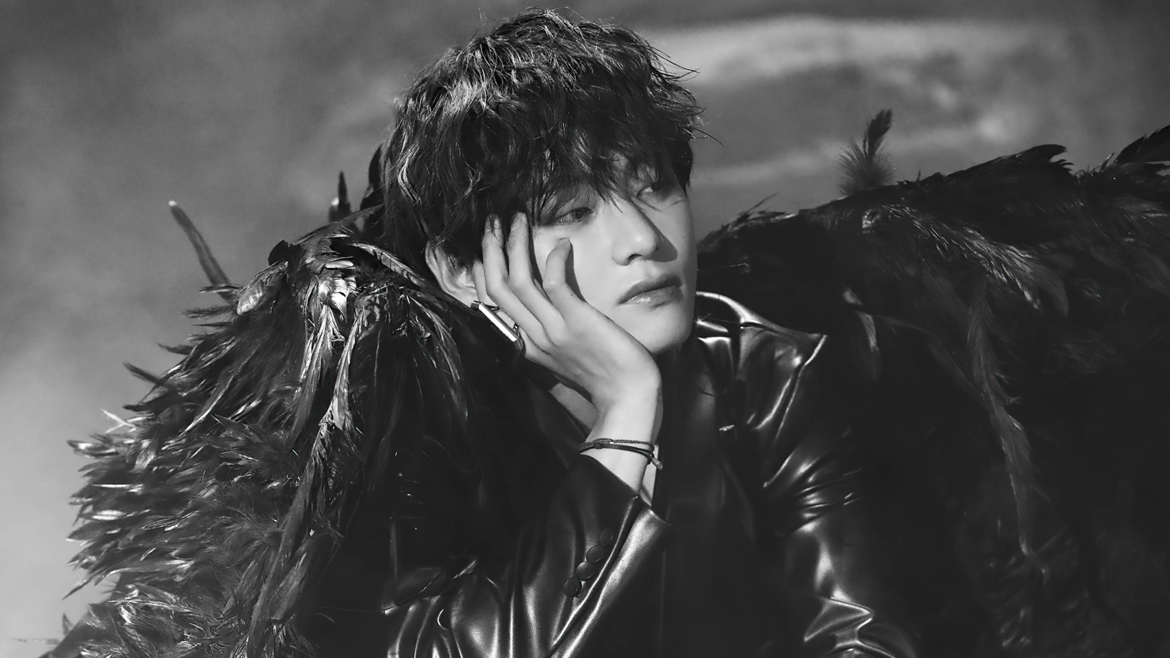 BTS 田柾國 黑色羽翼 壁紙 — 一個擁有深色羽毛翅膀的人，在戲劇性的黑白肖像中將手放在臉頰上。