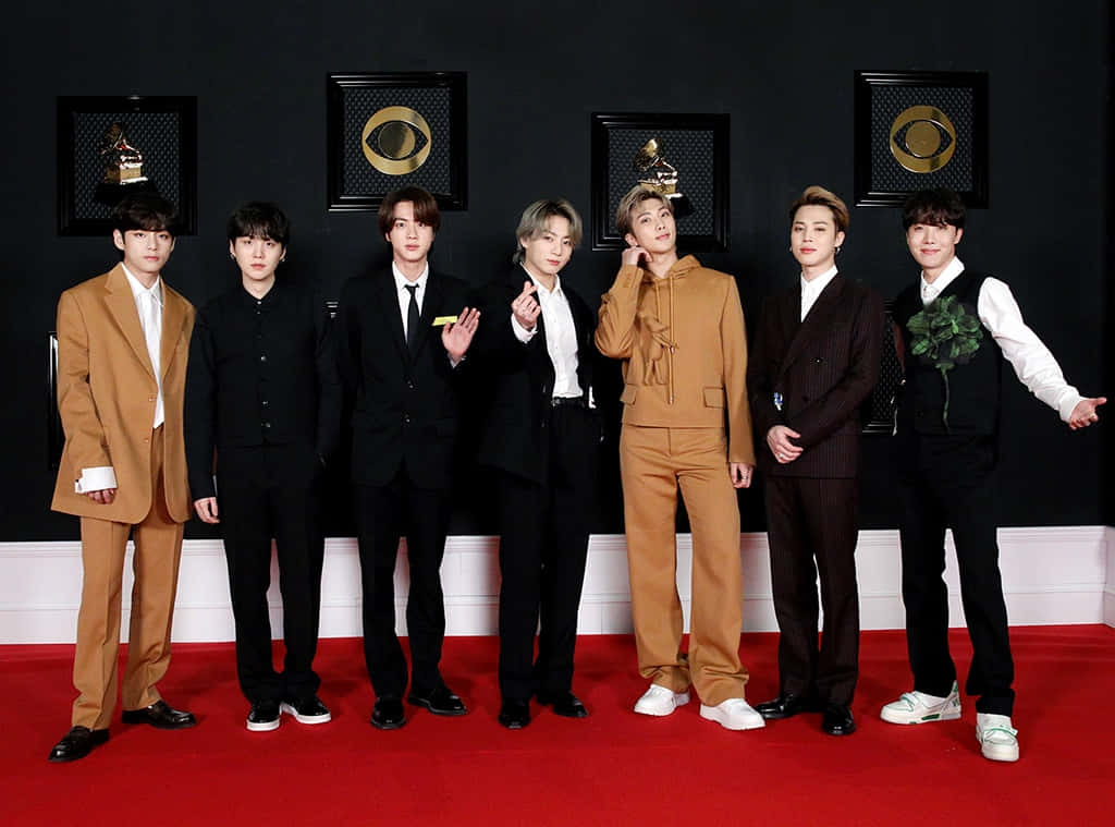 BTS 穿 Louis Vuitton 套裝照片 壁紙 — 七位穿著西裝的時尚男士在紅地毯上自信地擺姿勢，背景是裝飾著格林美獎項的黑色牆壁。