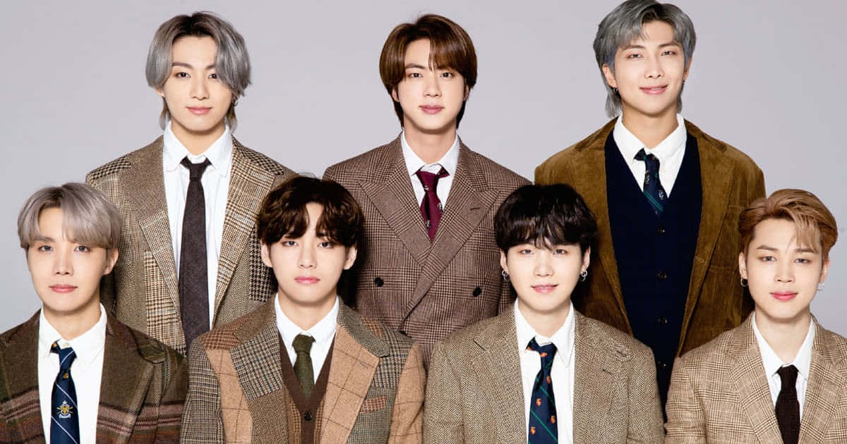 BTS 穿棕色西裝的可愛男孩團體寫真 壁紙 — 七位時尚年輕男士穿著協調的棕色格子西裝，在純灰色工作室背景前自信地擺姿勢。