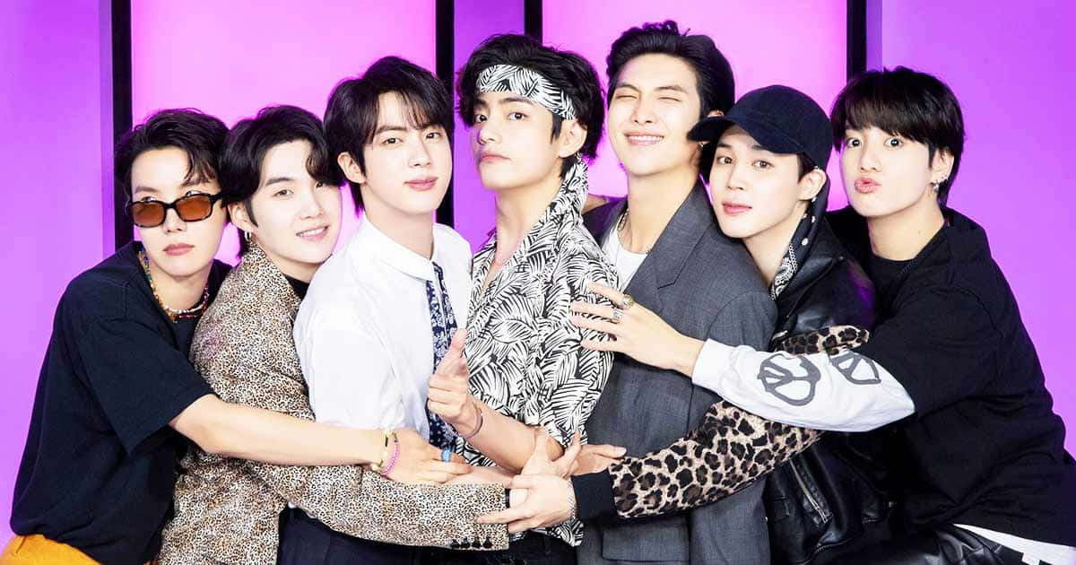 BTS 紫色背景團體照 壁紙 — 七位時尚年輕男子在充滿活力的紫色背景下緊密擺姿勢，穿著帶有醒目圖案和配飾的時尚折衷服裝。