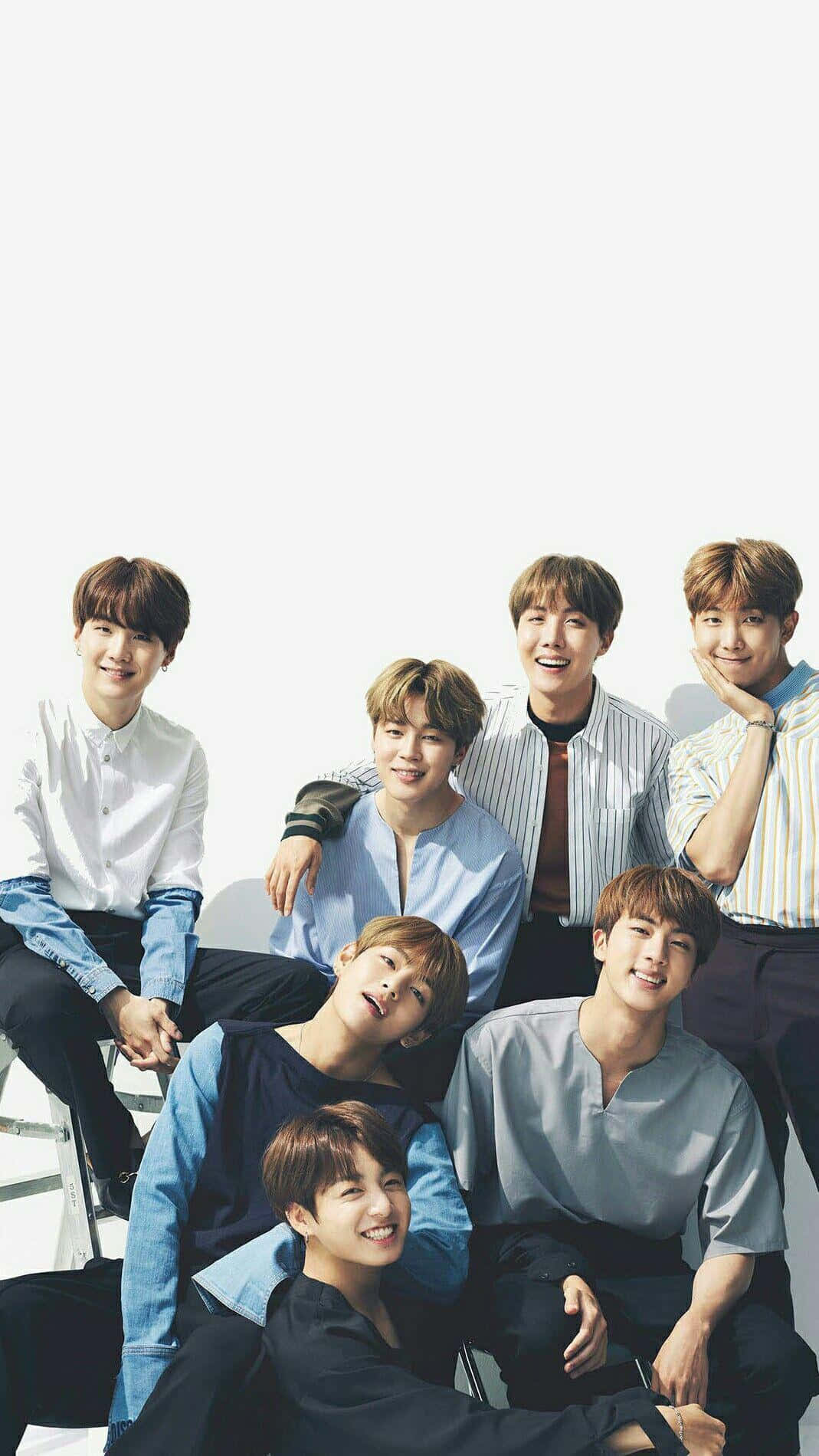 BTS 美學 iPhone 照片拍攝 壁紙 — 七位微笑的年輕男士穿著休閒襯衫，在明亮的白色背景前一起擺姿勢，展現俏皮的友誼。