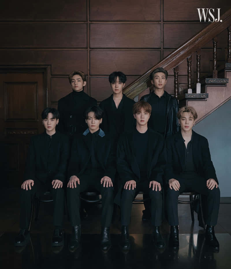 BTS《華爾街日報》肖像照 壁紙 — 七名身穿黑色西裝的男子在華麗的木樓梯背景下莊嚴地坐在椅子上。