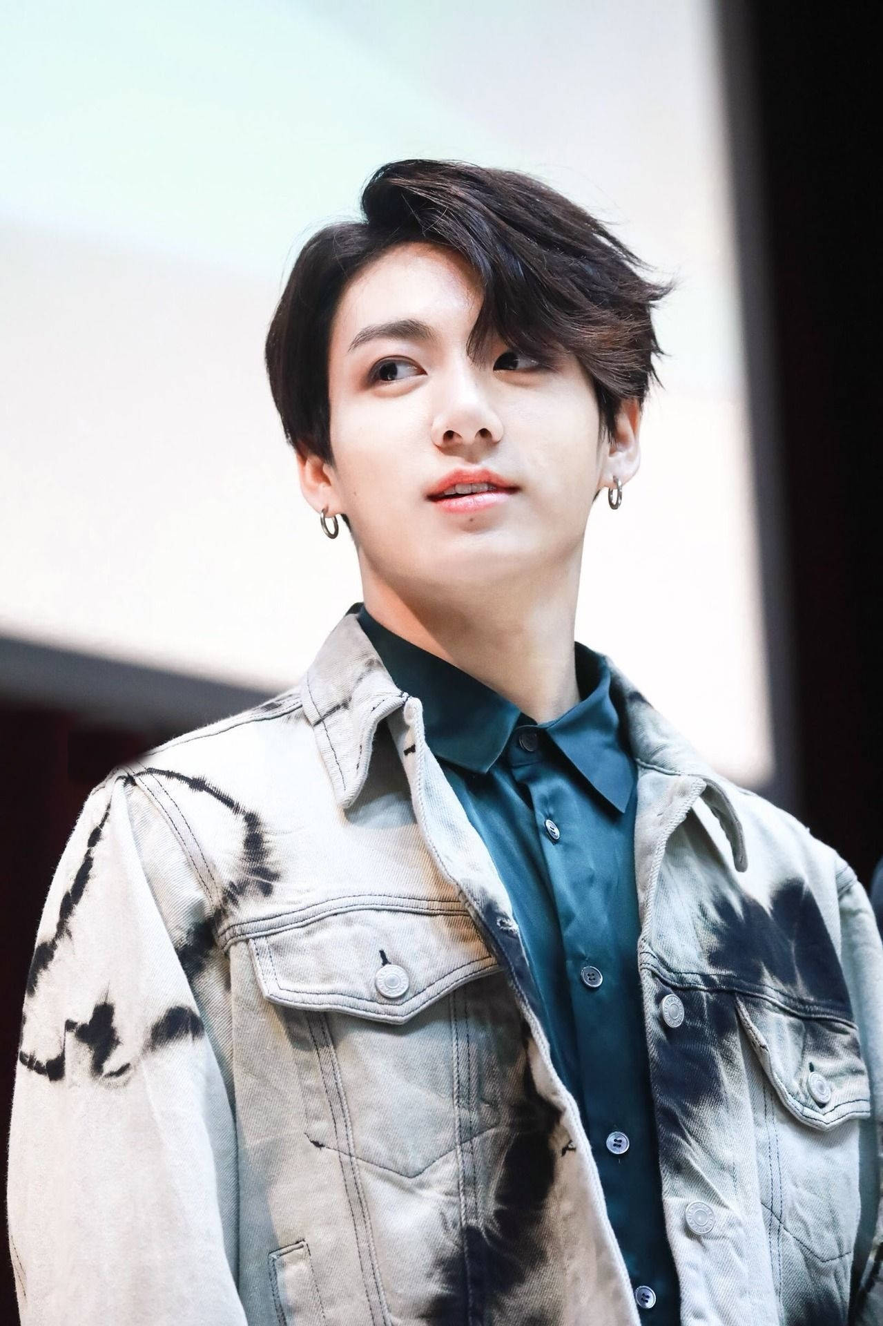 BTS 金俊勉 Aladdin 粉絲見面會 壁紙 — 一位黑髮戴耳環的年輕男子，身穿紮染牛仔外套配深色襯衫，向上仰望，表情柔和。