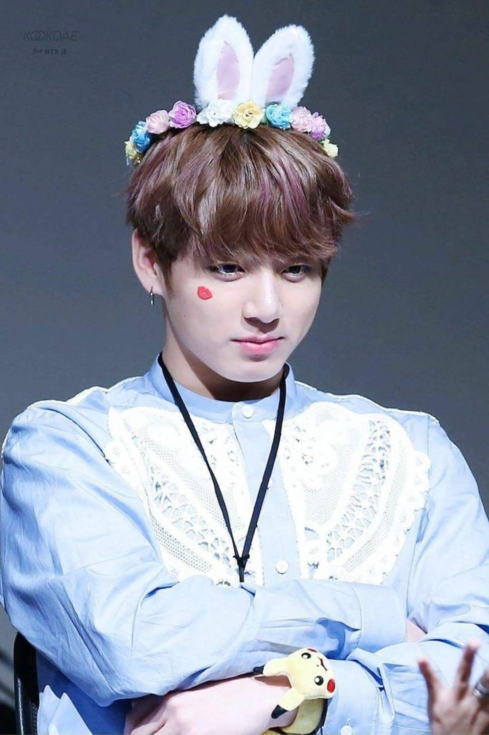 BTS 金俊勉 貓耳髮箍造型 壁紙 — 一位年輕男子戴著兔耳和花冠，穿著淺藍色蕾絲襯衫，抱著皮卡丘毛絨玩具。