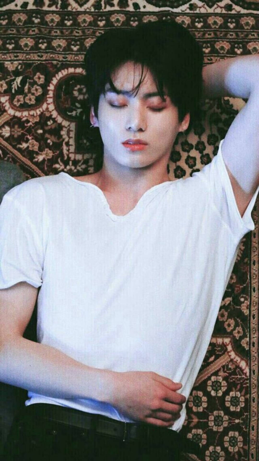 BTS 金俊奎 可愛地毯躺姿 壁紙 — 一名黑髮年輕男子身穿白色T恤，頭向後靠在華麗圖案地毯上。