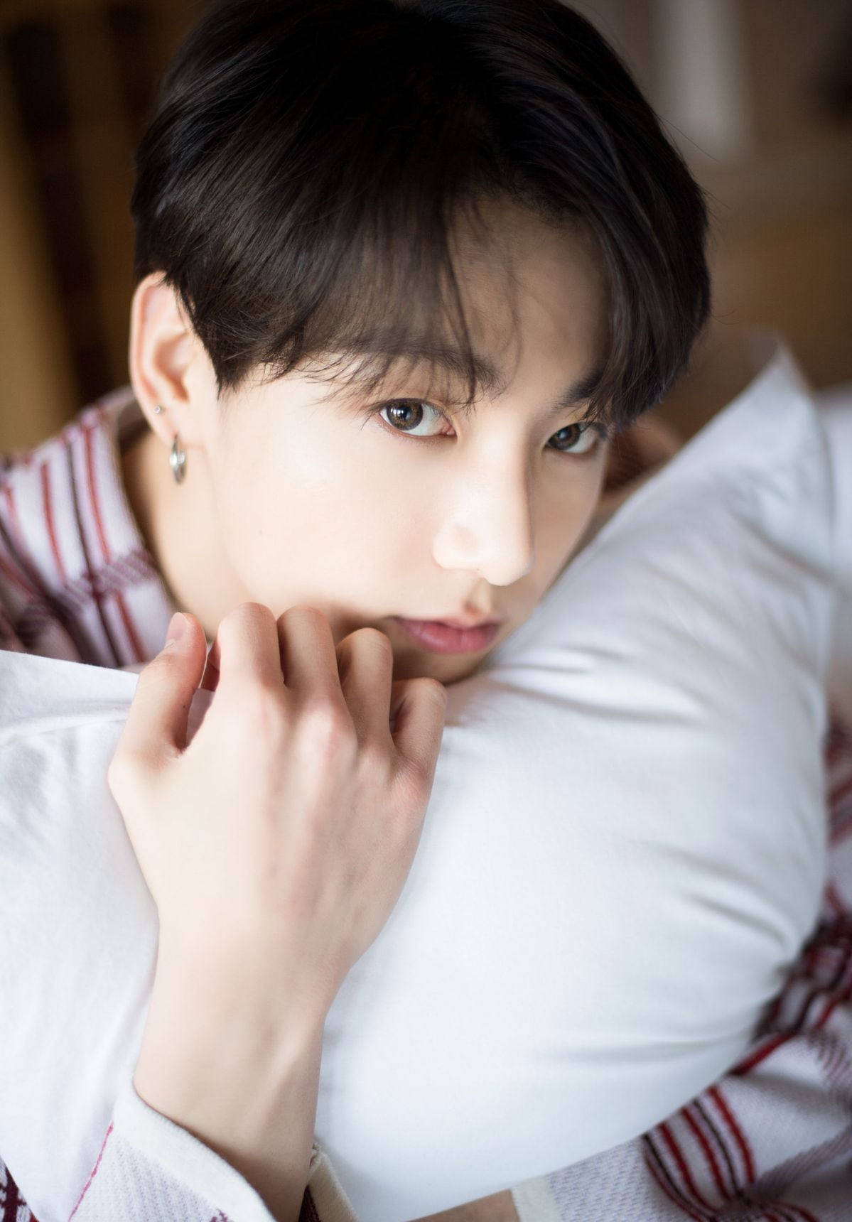 BTS 金俊奎 可愛抱枕造型 壁紙 — 一位黑髮年輕男子將頭靠在白色枕頭上，穿著紅白條紋襯衫，溫柔地凝視著。