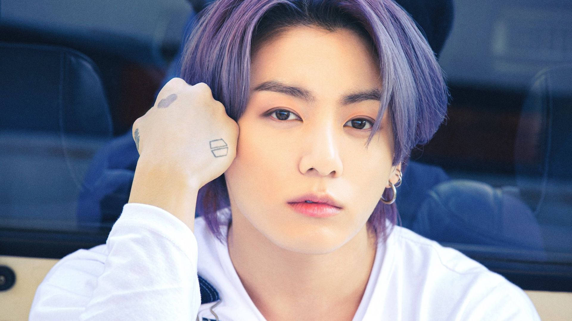 BTS 金泰亨凝視前方 壁紙 — 一位紫髮年輕男子在車內將紋身的拳頭抵在臉頰上，專注地凝視。