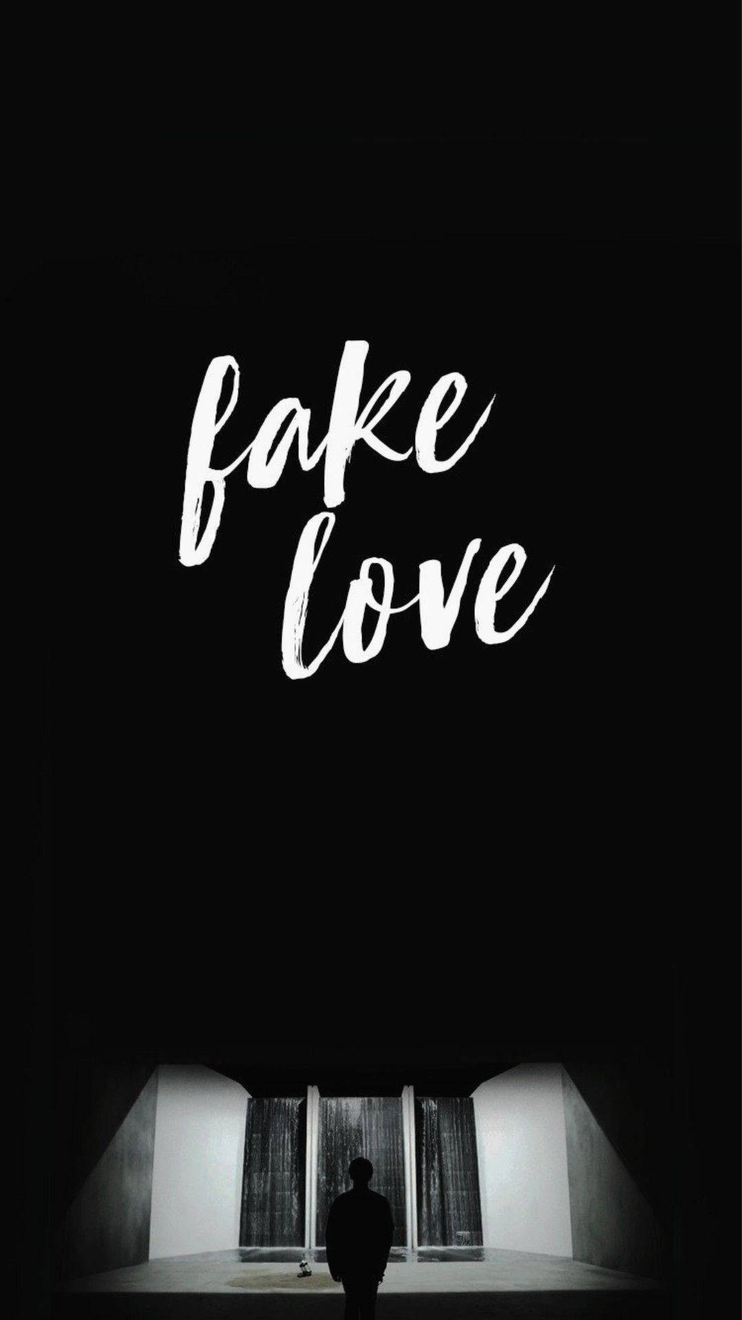 一個人在黑暗的房間裡獨自站在 'fake love' 字樣下方。
