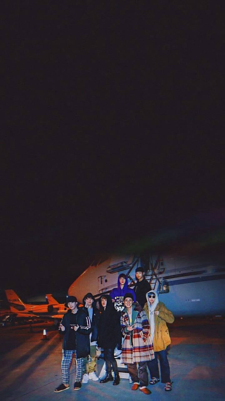 一群朋友在夜晚的機場停機坪上靠近飛機合照。