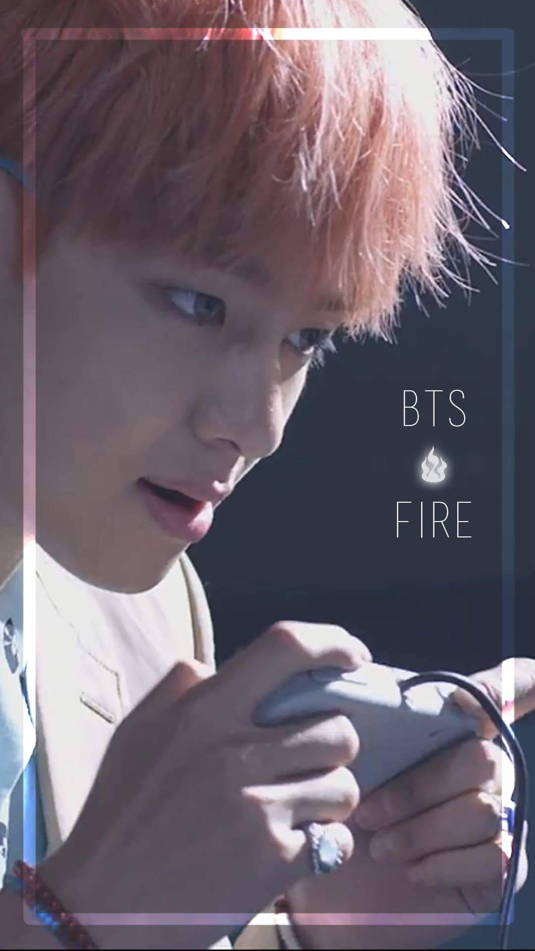 BTS泰亨《FIRE》 壁紙 — 一位粉紅色頭髮的年輕男子在明亮燈光下專注地玩手提遊戲機。