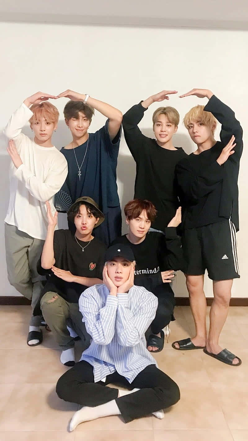 BTS可愛拍攝 壁紙 — 七位年輕男子在室內對著素色牆壁，雙手在頭頂做出形狀，擺出俏皮的姿勢。