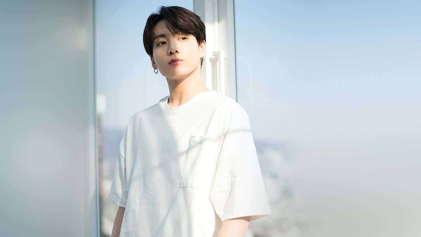BTS在皇室風寫真中閃耀奪目 壁紙 — 一位身穿白色T恤的年輕男子站在明亮的窗邊，身後的城市景觀模糊不清。