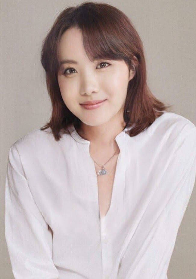 一位棕色頭髮的女性，身穿白色襯衫和項鍊微笑。