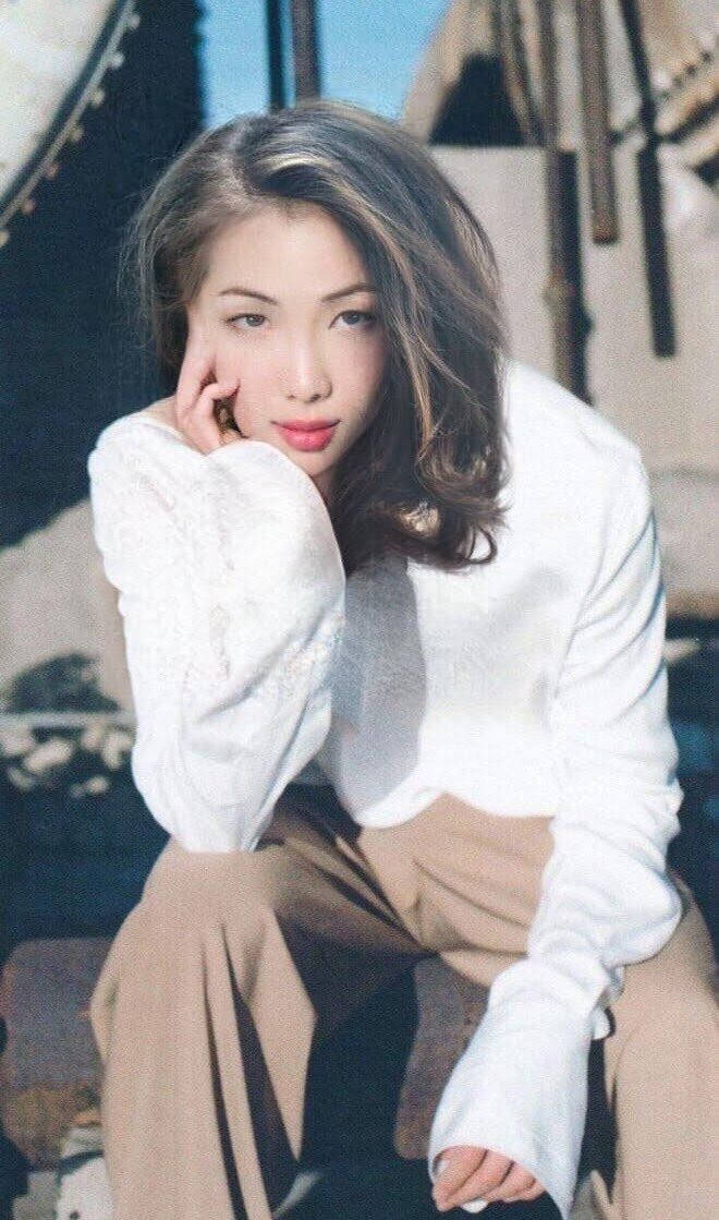 一位穿著白色襯衫和米色褲子的女性，在室內將手放在下巴下擺姿勢。