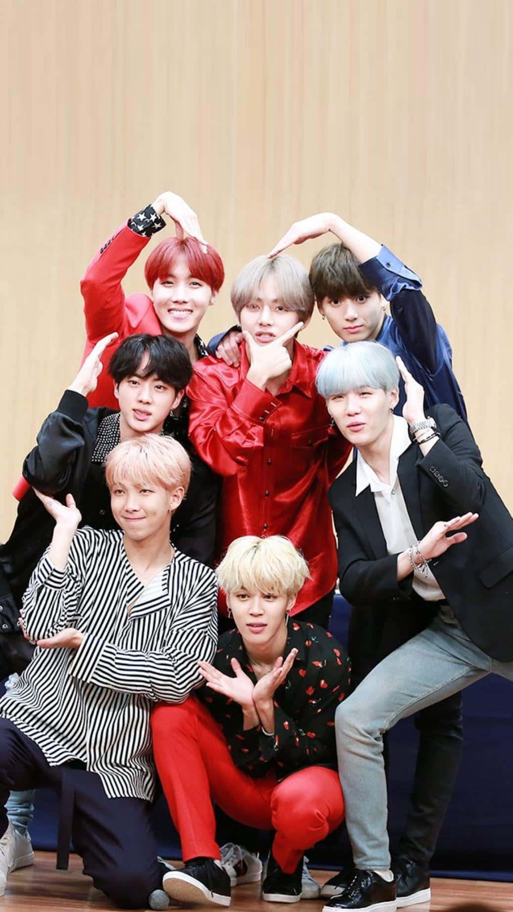 BTS心形iPhone壁紙 壁紙 — 七位時尚的年輕男子擁有色彩繽紛的頭髮，在木牆和明亮燈光的攝影棚中俏皮地擺姿勢。