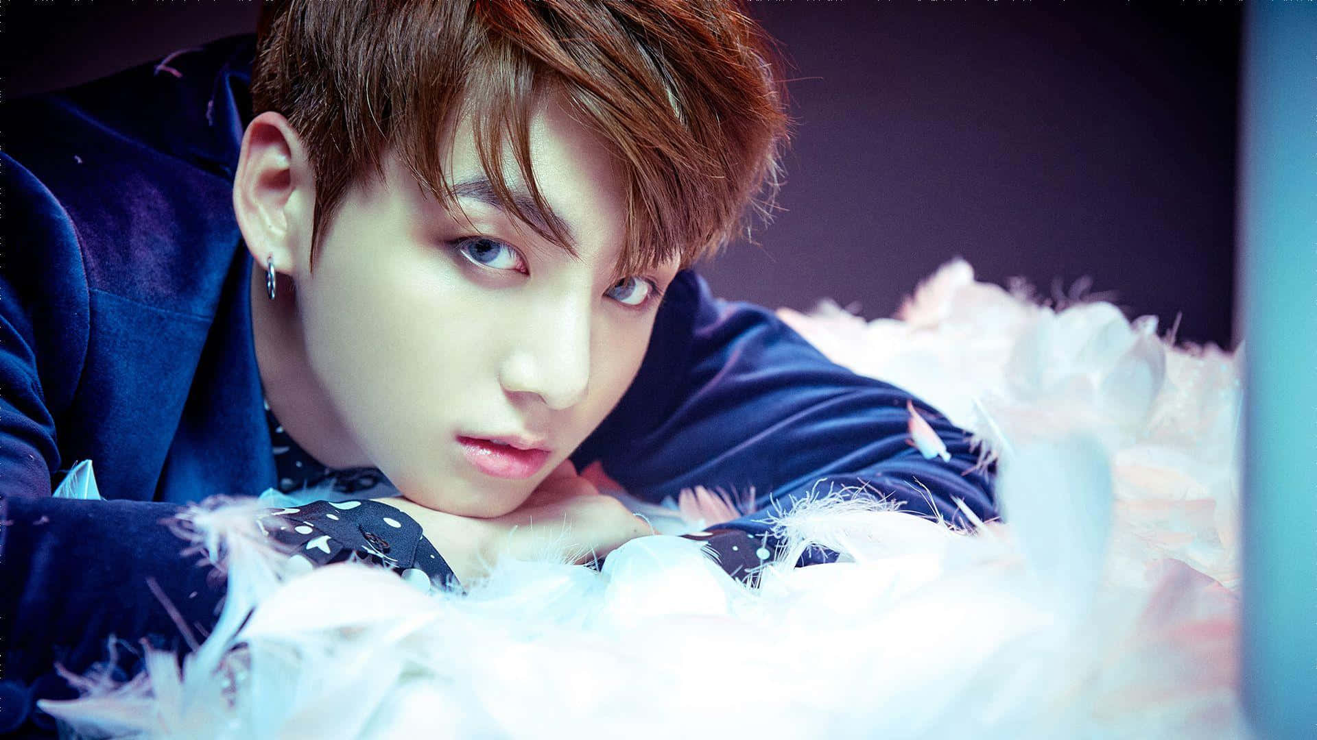 BTS成員Jungkook在旅程中尋找他的命運 壁紙 — 一位藍眼睛、棕色頭髮的年輕男子躺在白色羽毛上，穿著深藍色天鵝絨服裝。
