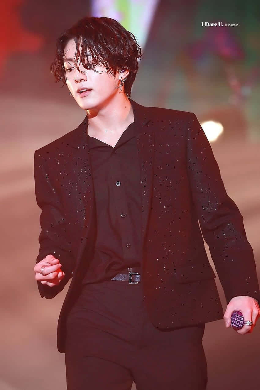 K-pop歌手身穿黑色閃亮西裝在舞台上手持麥克風表演。