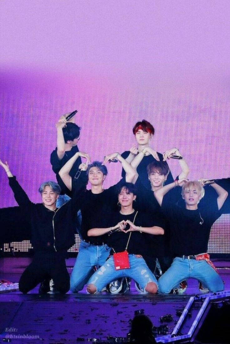BTS成員舞台心形手勢 壁紙 — 七位男K-pop偶像在充滿活力的紫色燈光下在舞台上充滿活力地擺姿勢，用手形成心形。