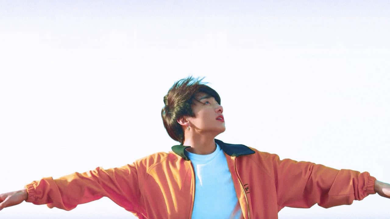 BTS才華洋溢的歌手兼詞曲創作人Jungkook 壁紙 — 一個穿著橙色外套的年輕人張開雙臂，面向明亮的白色天空，頭部向上傾斜，感受自由。