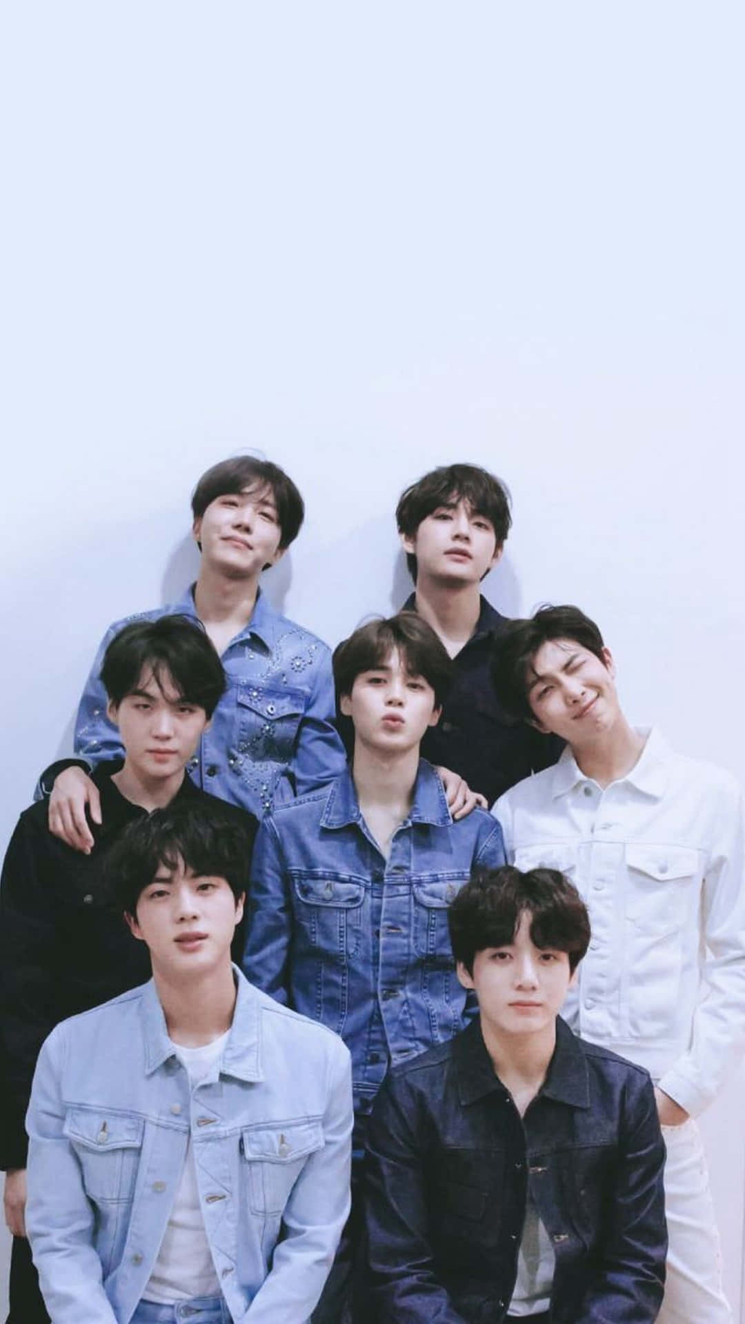 BTS攝影棚 iPhone壁紙 壁紙 — 七個年輕男子身穿牛仔外套，在柔和燈光下隨意地靠著白牆擺姿勢。