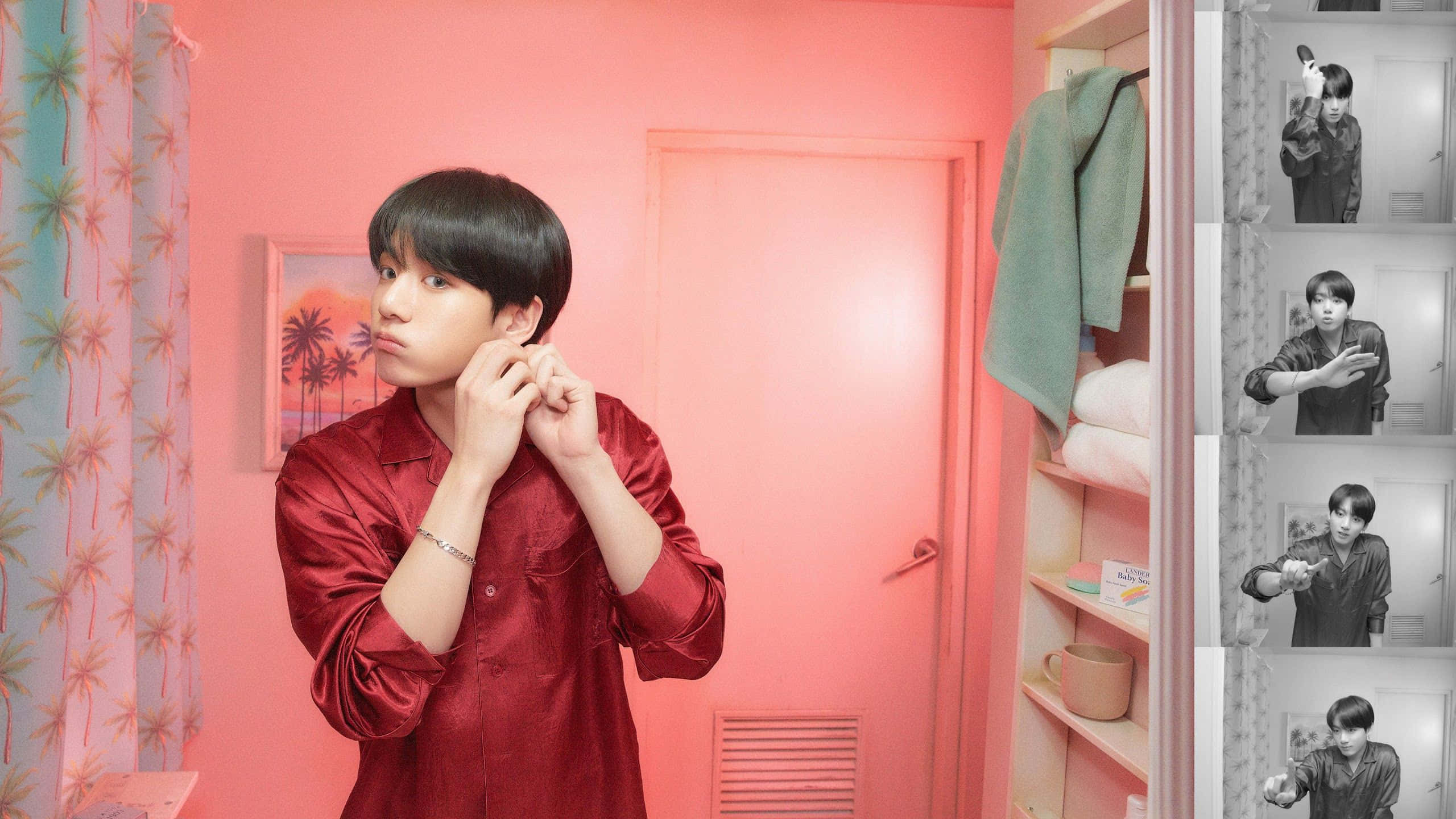 BTS明星展示最新Mac產品 壁紙 — 一位身穿紅色緞面襯衫的年輕男子在一個粉紅色房間內調整耳機，房間有棕櫚圖案窗簾和一個展示黑白動作照片的衣櫃。
