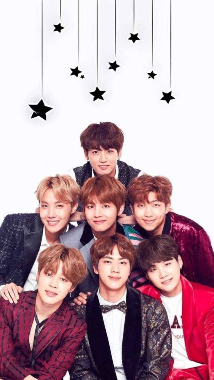 BTS星星可愛風 壁紙 — 七位面帶微笑的年輕男士身著時尚西裝，在白色背景懸掛的黑色星星下一起擺姿勢。