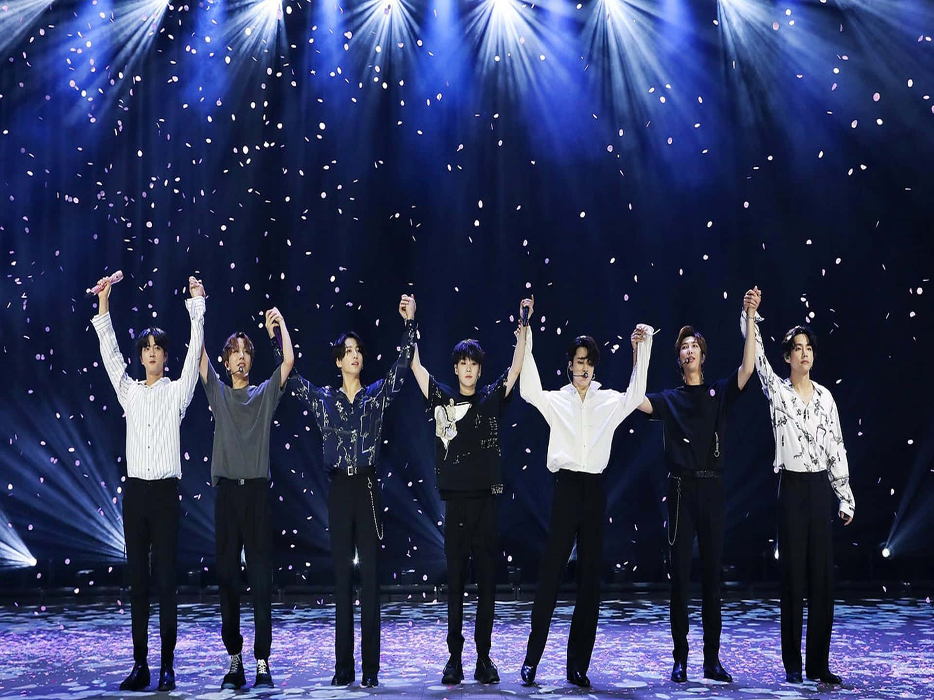 BTS樂團舞台表演燈光 壁紙 — 七位男表演者在舞台上排成一排，在明亮的藍色聚光燈下，白色紙屑飄落。