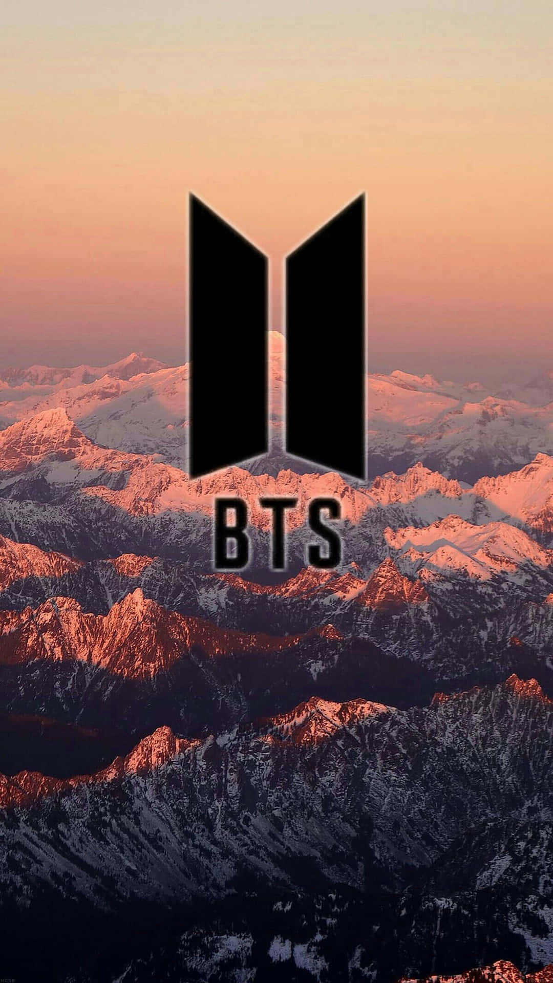 BTS標誌iPhone壁紙 壁紙 — BTS標誌在溫暖的日落色調中，雄偉地矗立在白雪覆蓋的山脈前。