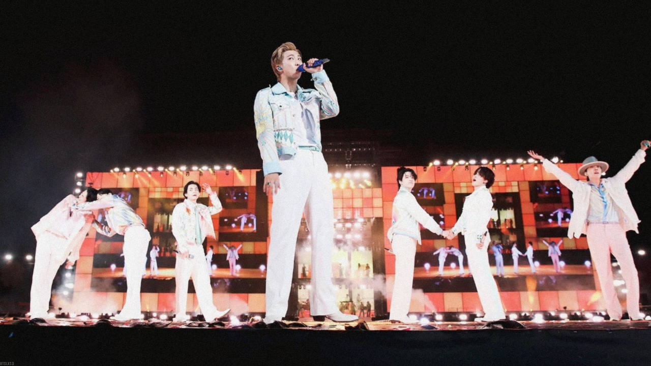 K-pop團體在夜晚燈光舞台上表演同步舞蹈動作。