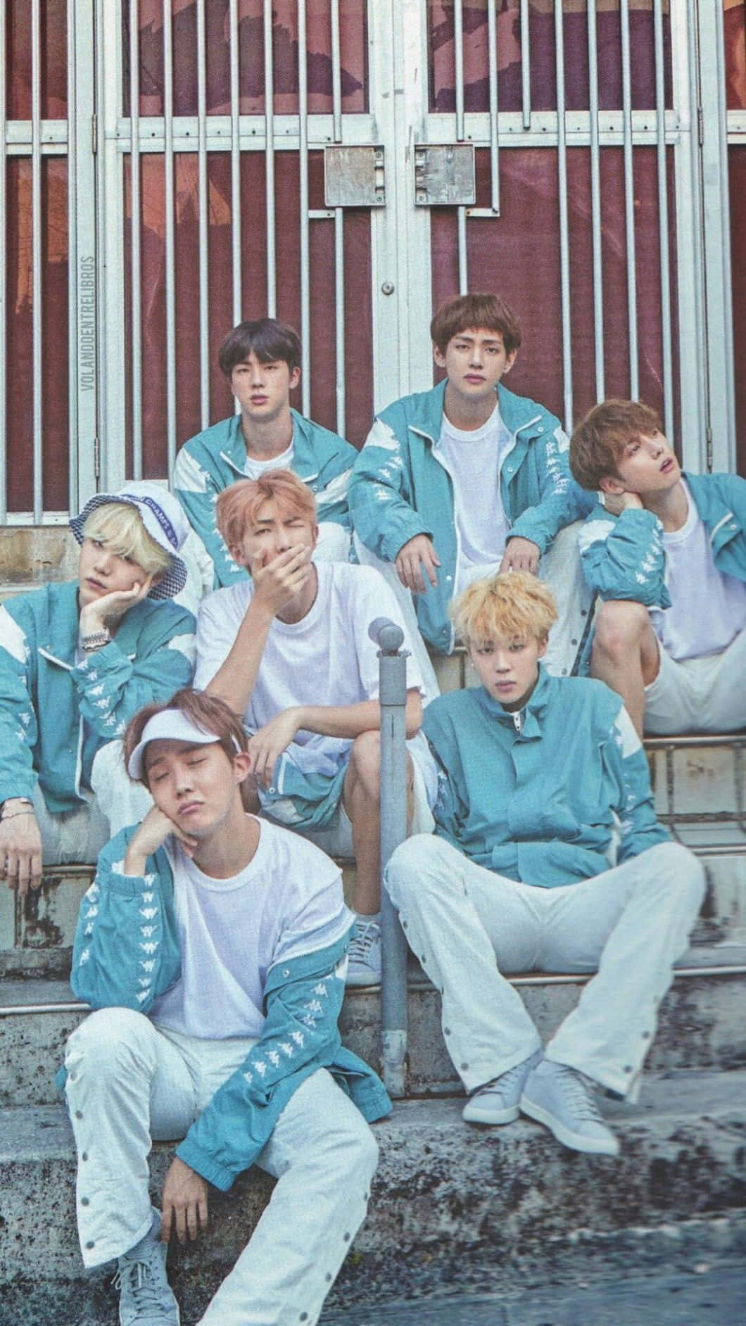 BTS牛仔iPhone壁紙 壁紙 — 七名年輕男子身穿相配的青綠色外套和白色T恤，在生鏽的金屬門前風化的混凝土台階上隨意擺姿勢。