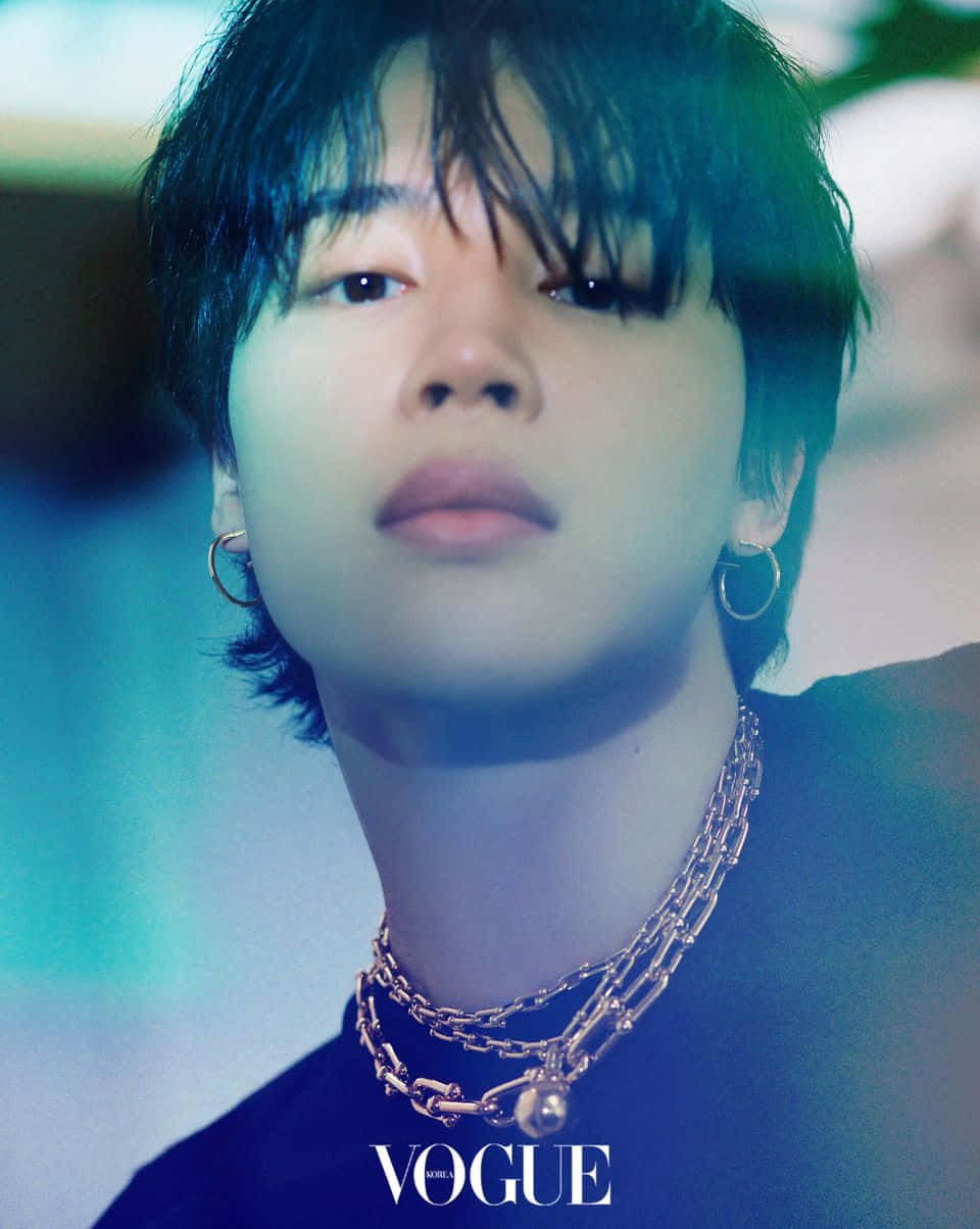 BTS的Jimin展現迷人魅力 壁紙 — 一位黑髮、戴著金色圓環耳環的年輕男子在冷藍色燈光下直視鏡頭，穿著多層鏈條項鍊和深色上衣。