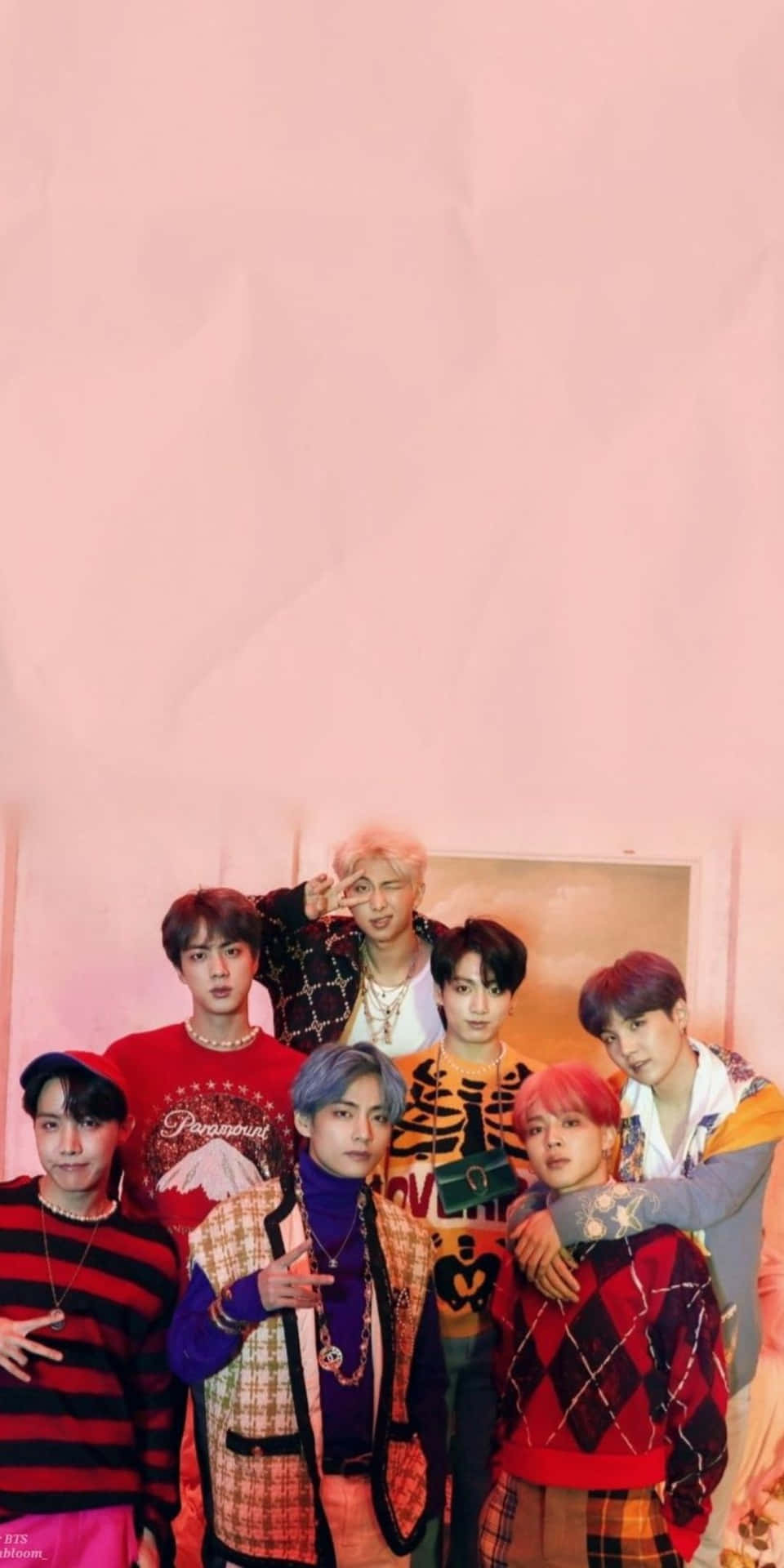 BTS穿酷炫圖案拍攝 壁紙 — 七位時尚年輕男士身穿色彩繽紛的圖案服裝，在柔軟的粉紅色紋理牆前自信地擺姿勢。