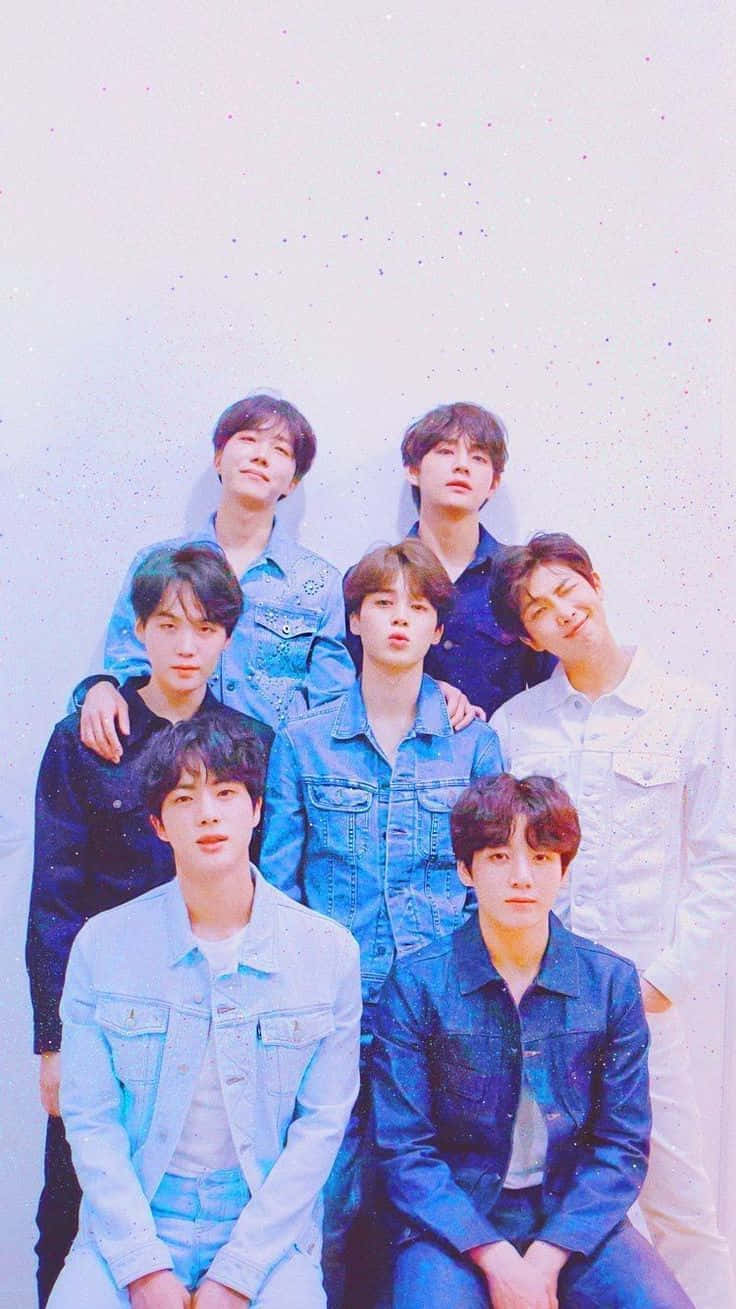 BTS身穿牛仔夾克拍攝寫真 壁紙 — 七個穿著牛仔外套的年輕男子在柔和的粉彩背景前一起擺姿勢，背景帶有微妙的閃亮斑點。