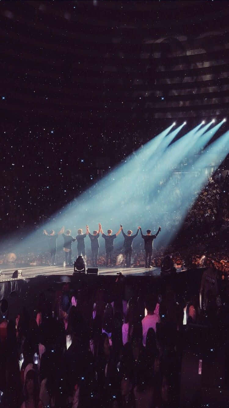 BTS韓國男子團體演唱會舞台背景 壁紙 — 七位表演者站在音樂會舞台上，在明亮的聚光燈下高舉雙臂，五彩紙屑落在歡呼的人群上。