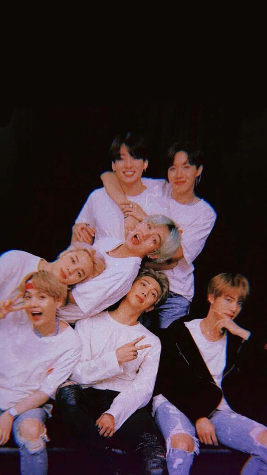 BTS黑色iPhone壁紙 壁紙 — 七名身穿白襯衫和破洞牛仔褲的年輕男性在黑色背景前以鮮豔燈光嬉戲擺姿勢。