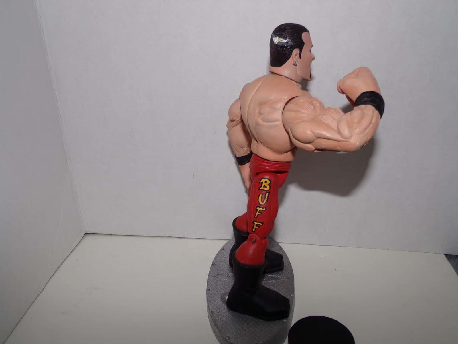 Buff Bagwell 拳擊手動作玩偶照片 壁紙 — 一個肌肉發達的摔角手動作人偶，穿著帶有黃色「BUFF」字樣的紅色褲子，展示其肱二頭肌。