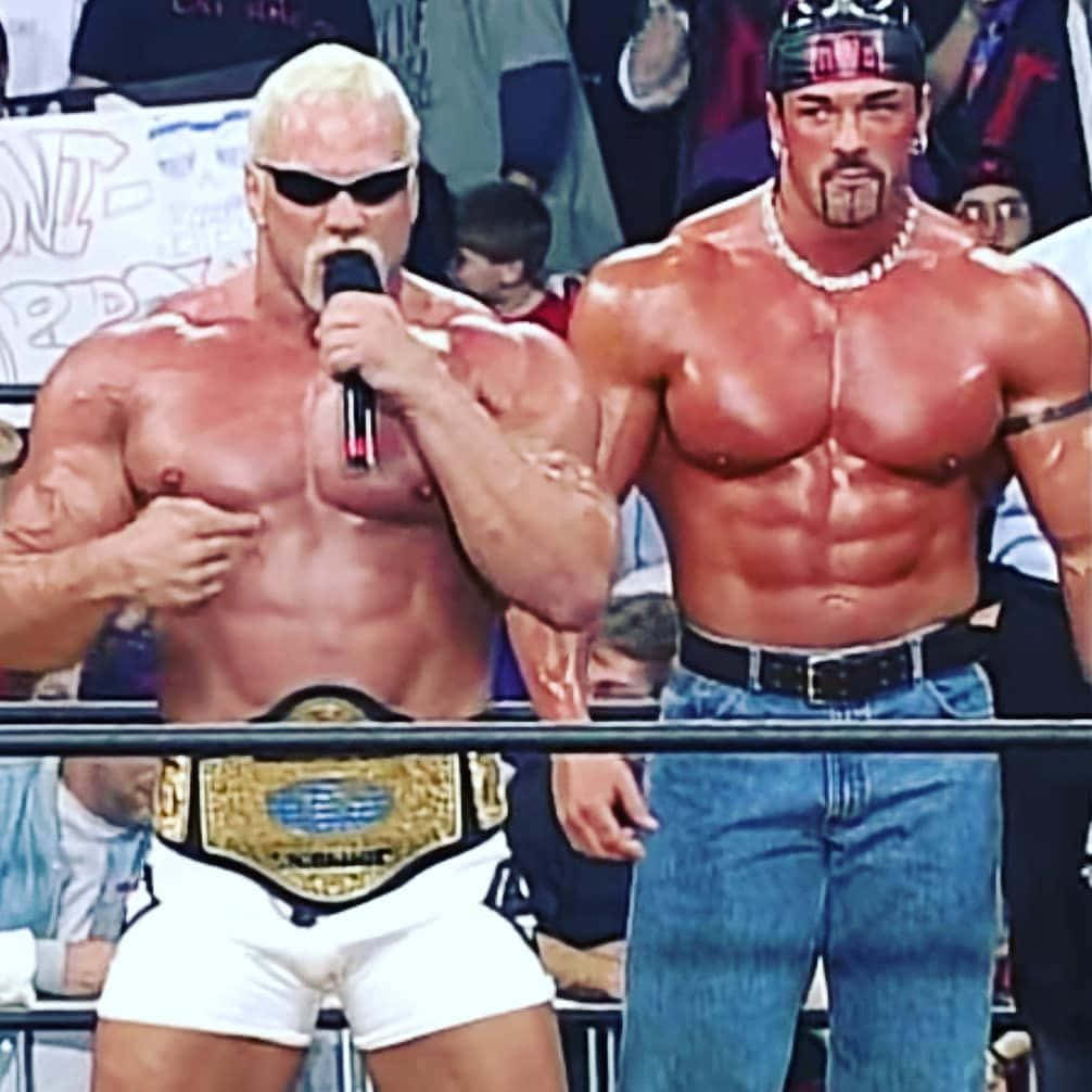 Buff Bagwell與Scott Steiner WWE傳奇攝影 壁紙 — 兩名肌肉發達的摔角手在擂台上，一人手持咪高峰並戴著冠軍腰帶，另一人穿著牛仔褲，兩人均赤裸上身，在明亮的場館燈光下。