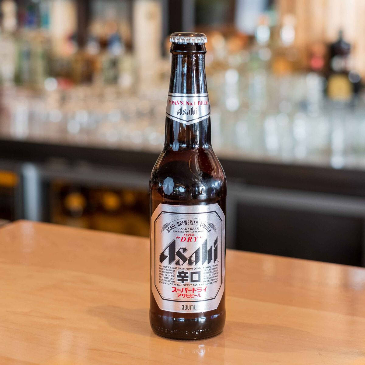 Asahi Super Dry 啤酒瓶放在木吧檯上，背景模糊的酒吧。