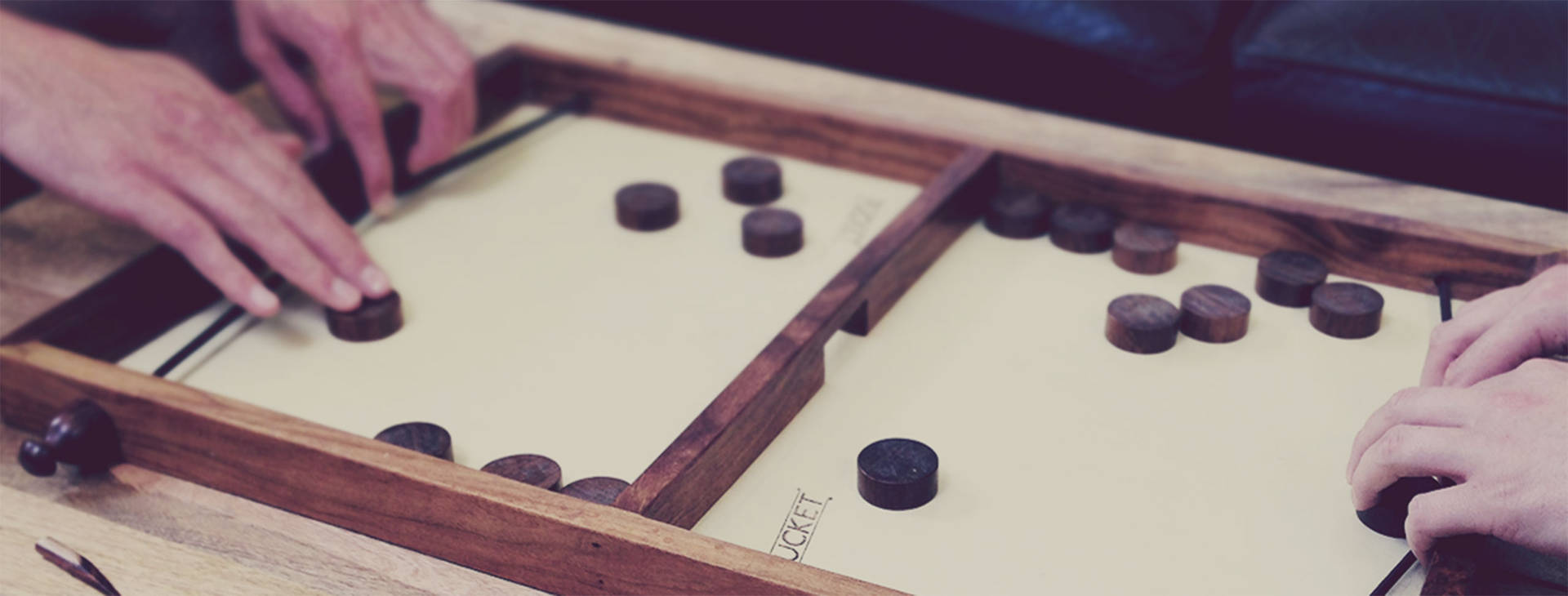 兩隻手在玩一個帶有深色圓盤的木製策略棋盤遊戲。