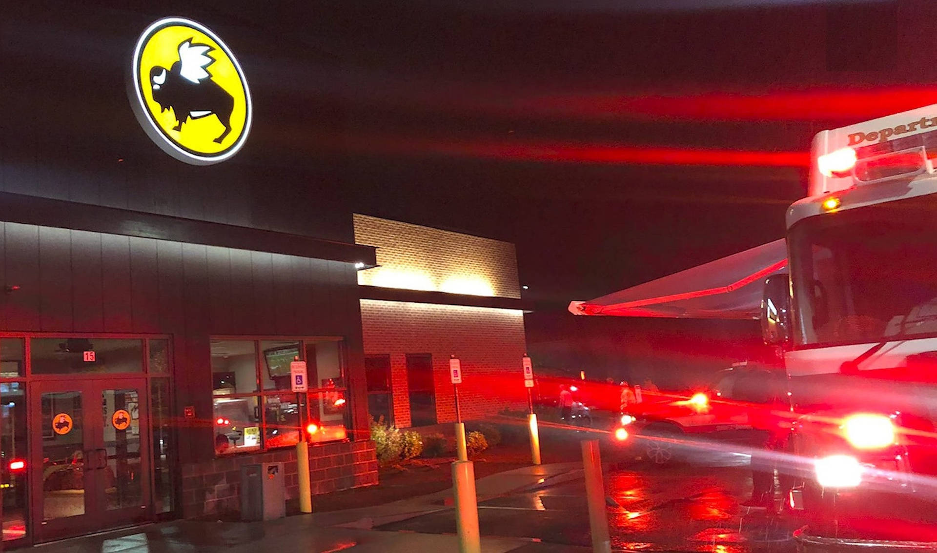 紅色尾燈在夜晚濕漉漉的街道上劃過Buffalo Wild Wings餐廳。