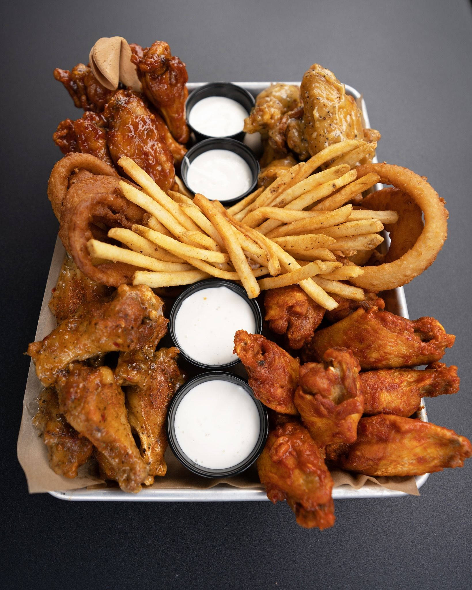 Buffalo Wild Wings 盛宴 壁紙 — 一個金屬托盤上堆滿了香脆的水牛城雞翼、洋蔥圈和金黃薯條，周圍放著四個小杯的奶油白色蘸醬。