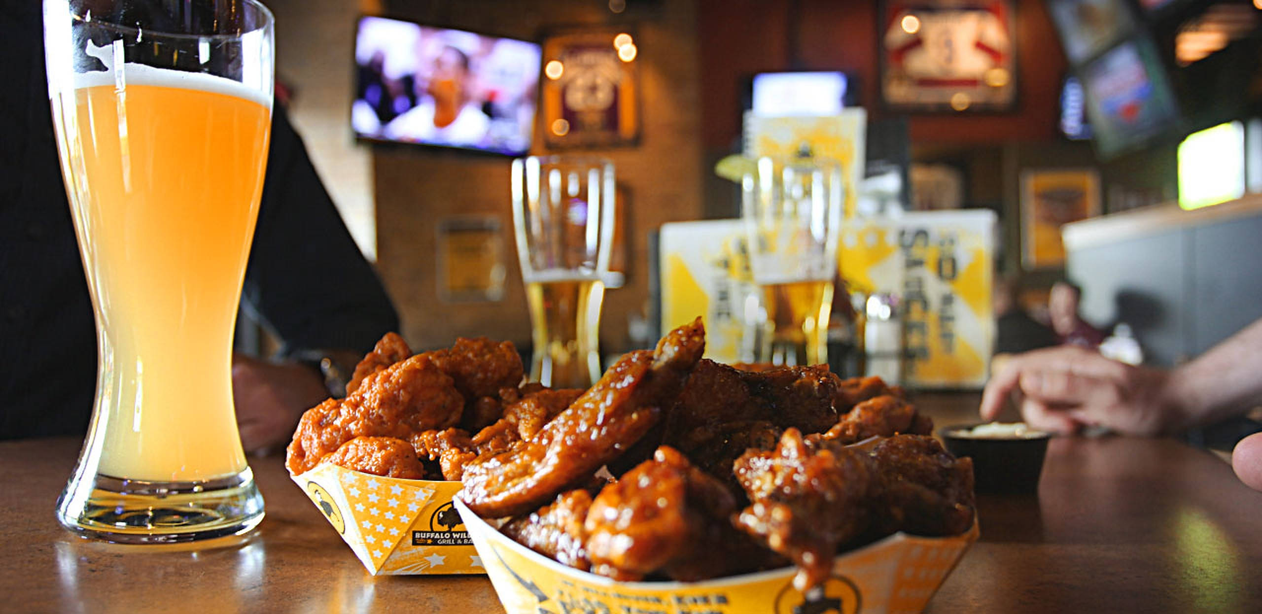Buffalo Wild Wings 餐廳場景 壁紙 — 一個充滿活力的運動酒吧中，木製吧枱上嘅脆皮水牛雞翼同高身啤酒杯嘅特寫。