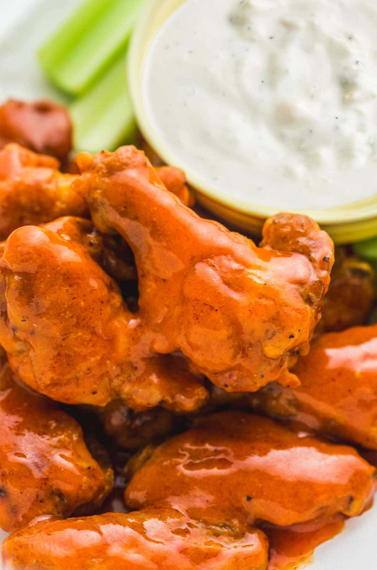 Buffalo Wild Wings 的熱鬧足球之夜 壁紙 — 脆皮水牛城雞翼在辣醬中閃閃發光，配以芹菜條和奶油蘸醬，放在白色碟子上。